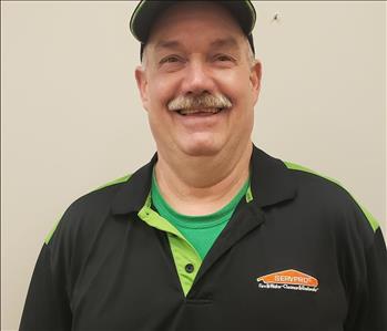 Man with hat smiling in front of beige background